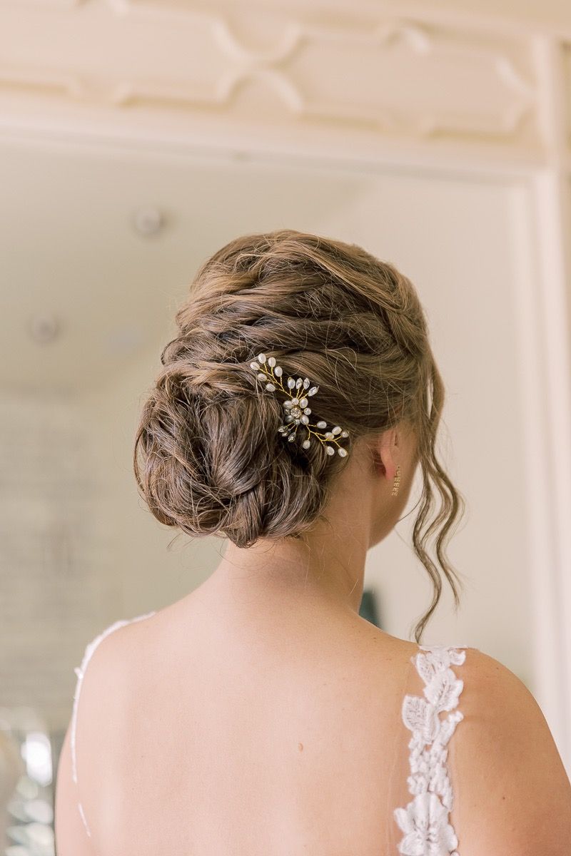 Brunette bride with woven bridal updo hairstyle, pearl floral hairpiece, and soft curls, styled elegantly for her wedding.